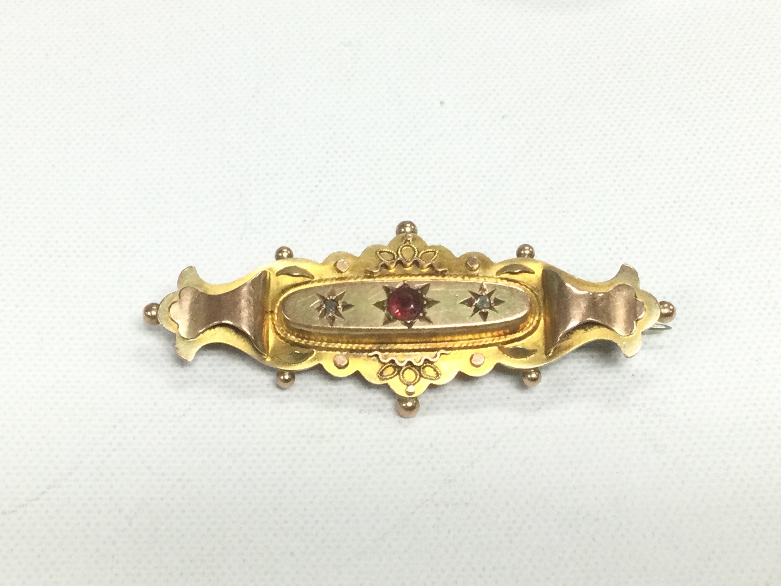 A 9ct gold brooch set with two small diamonds and a central ruby, approx 2.8g. Shipping category A.