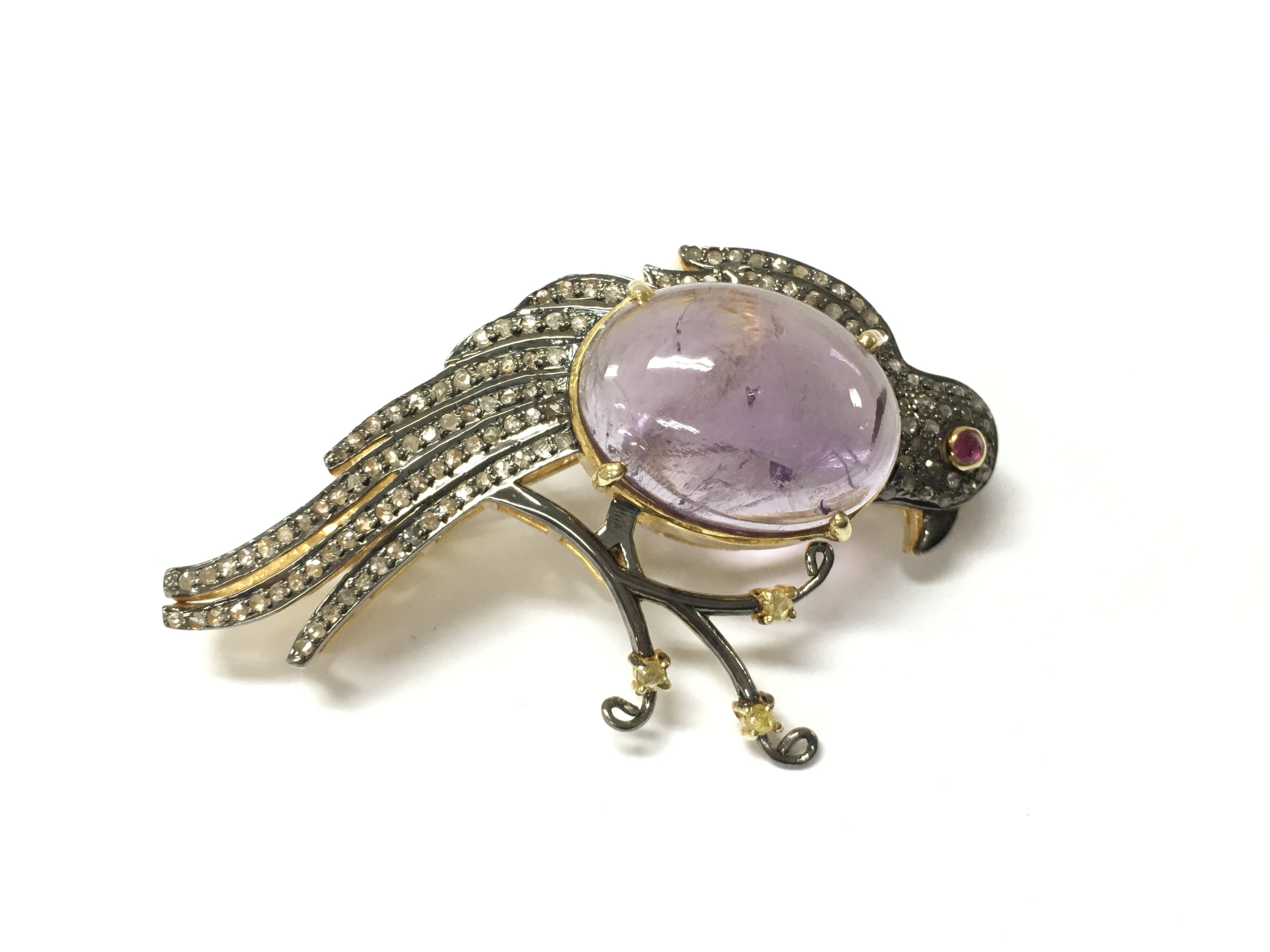 A large silver gilt bird of paradise brooch which can double as a pendant set with a large oval cabochon amethyst rose and round cut diamonds and a ruby. Fitted with a hinged pin and loop. Amethyst 12.30ct and diamonds 1.17ct. Approximately 5.5cm wide