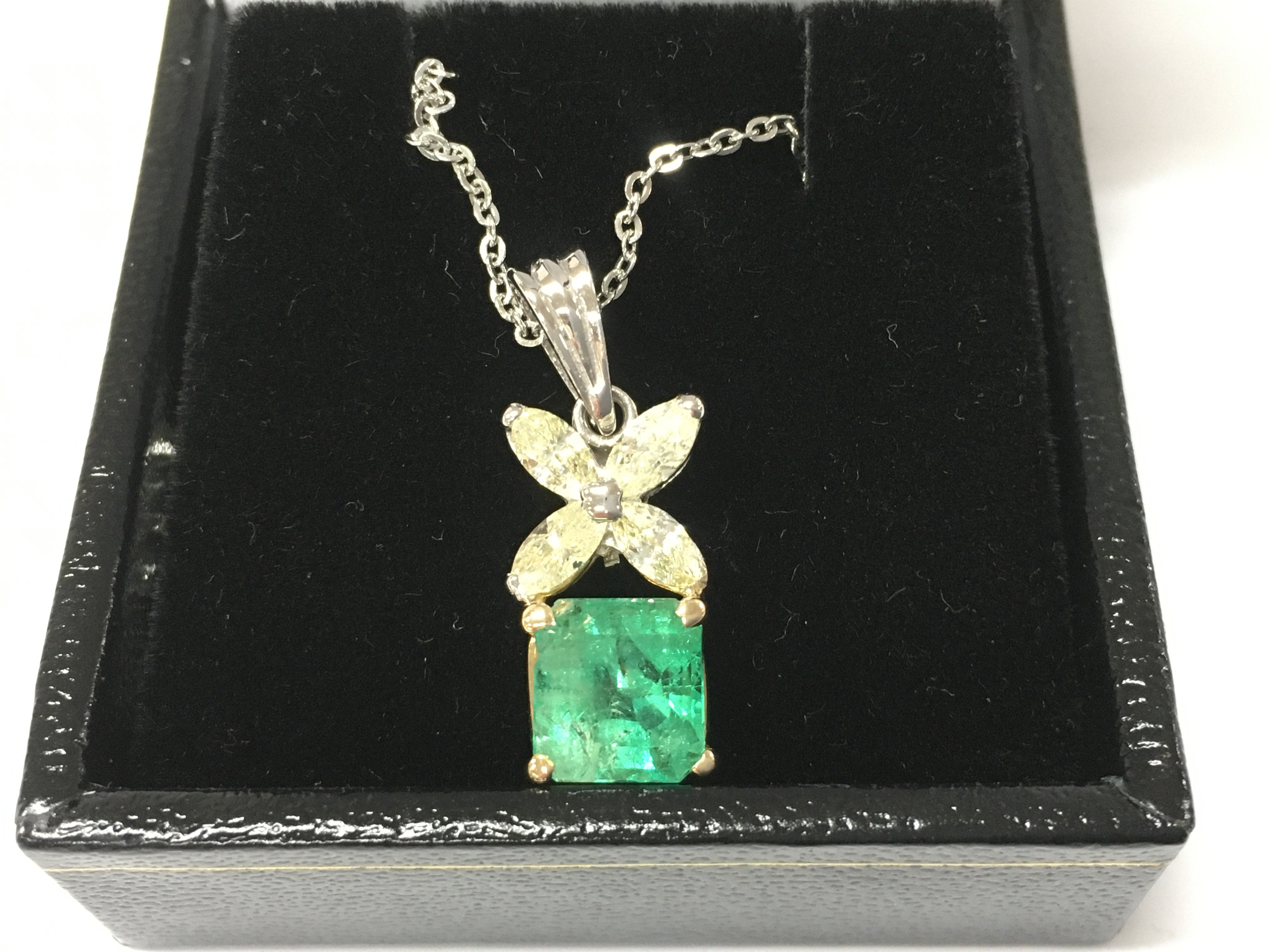 An 18ct white and yellow gold pendant set with square step cut emerald beneath 4 marquise cut diamonds on a silver chain. Emerald 1.25ct approx and 0.80ct diamonds approx. Postage B