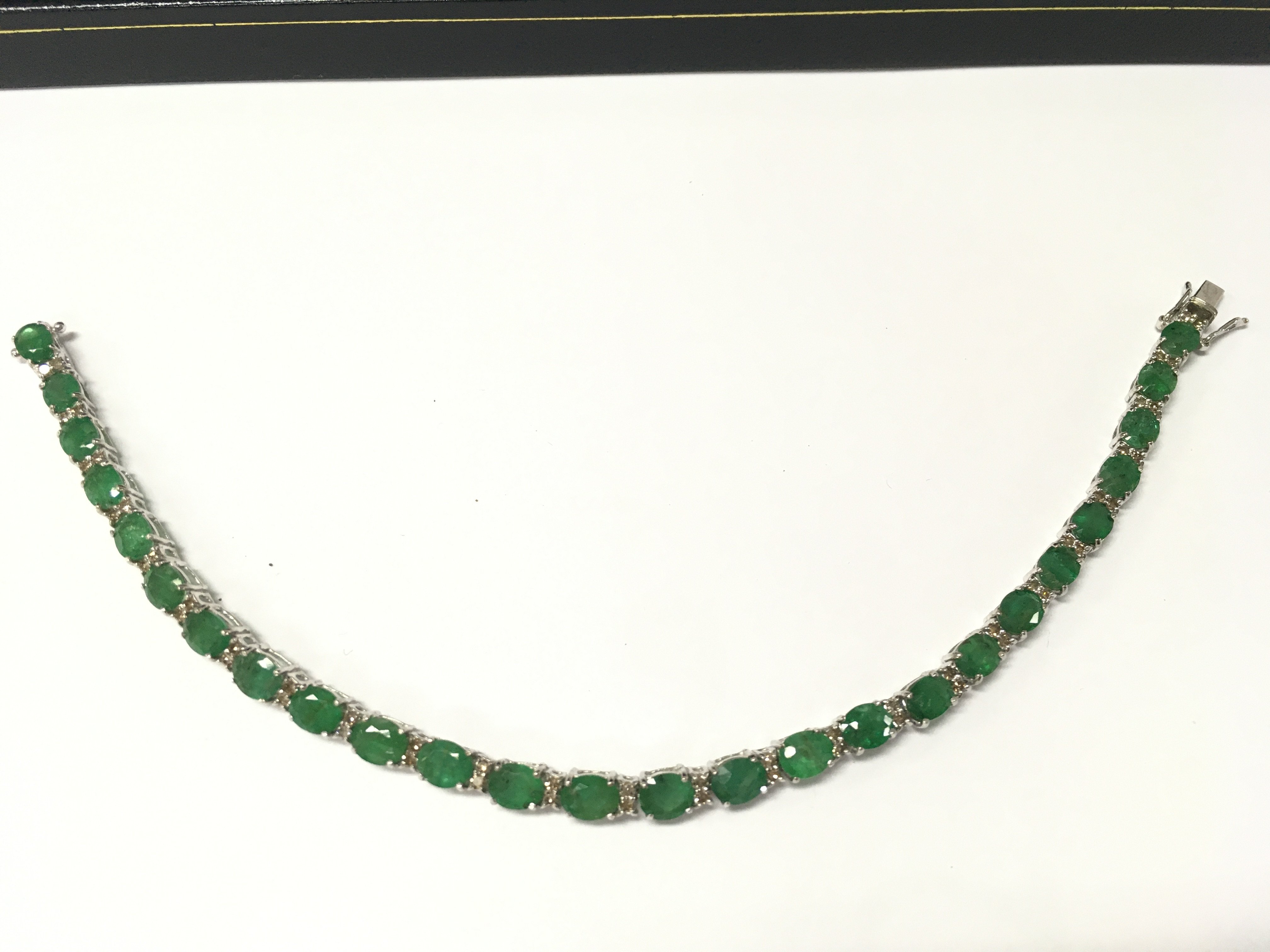 An 18ct white gold oval emerald and diamond line bracelet with an open box clasp and double safety catch. Emeralds 7.88ct and diamonds 0.55ct. Approx 18cm long. Postage B