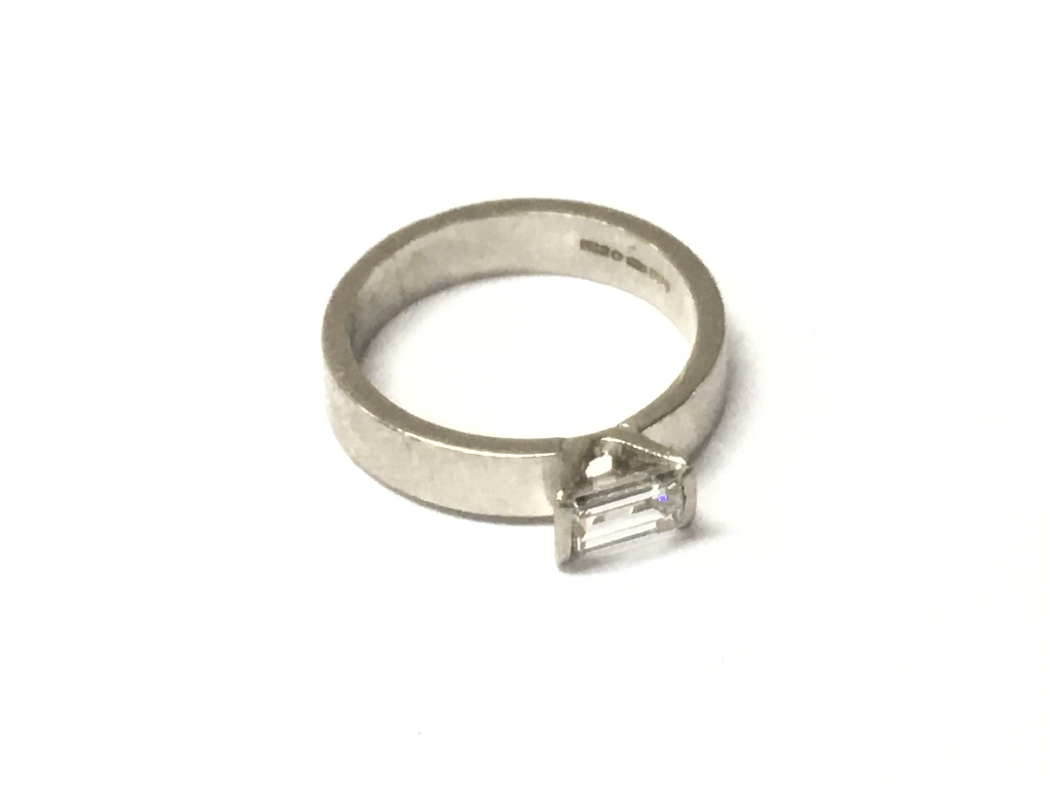 A platinum solitaire ring set with a rectangular cut diamond Approx 0.61cts. Approx weight 6.53 grams, size L.