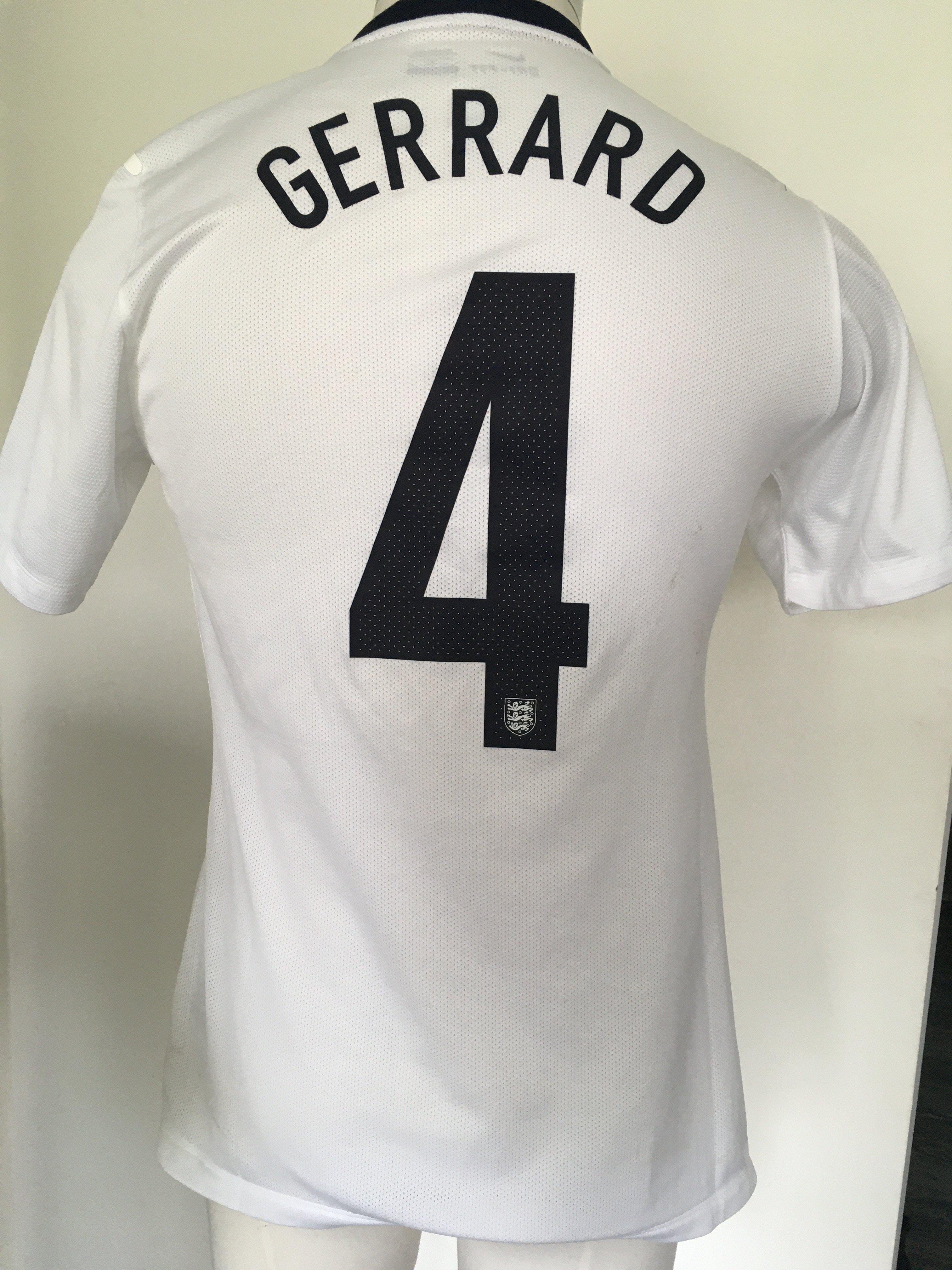 Steven Gerrard England Match Worn Football Shirt: White short sleeve shirt with number 4 Gerrard to rear. Front has number 4 and gold emblem below 3 Lions stating 150 years 1863 - 2013. Worn v Denmark in a friendly at Wembley on 5 3 2014. Photograph of Gerrard wearing the shirt which has matching stains.