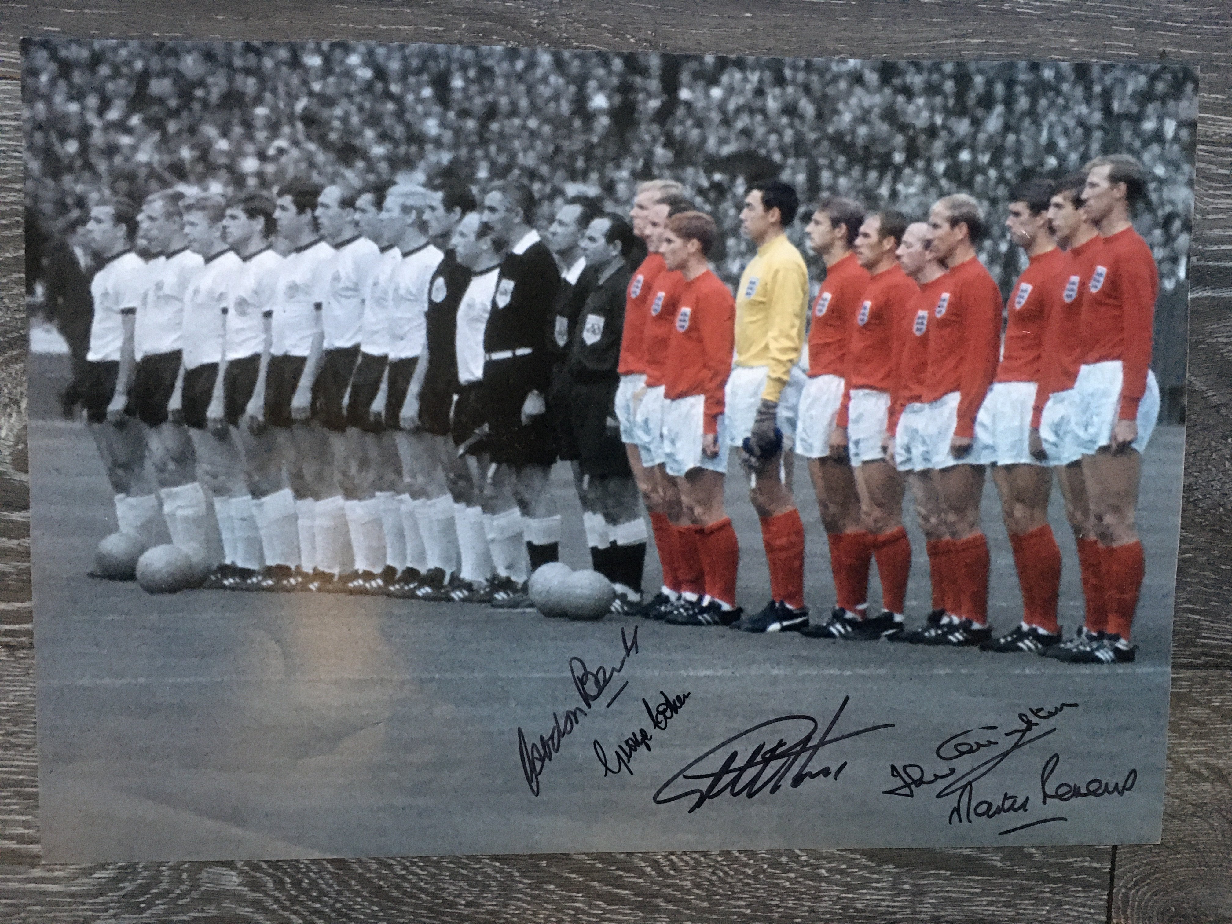 England 1966 World Cup Signed Football Print: Both teams lining up before the final with England players in colour and the rest of the print is black and white. Hand signed clearly in black marker pen by Peters, J Charlton, Hurst, Cohen and Banks. Measures 16 x 11 inches.