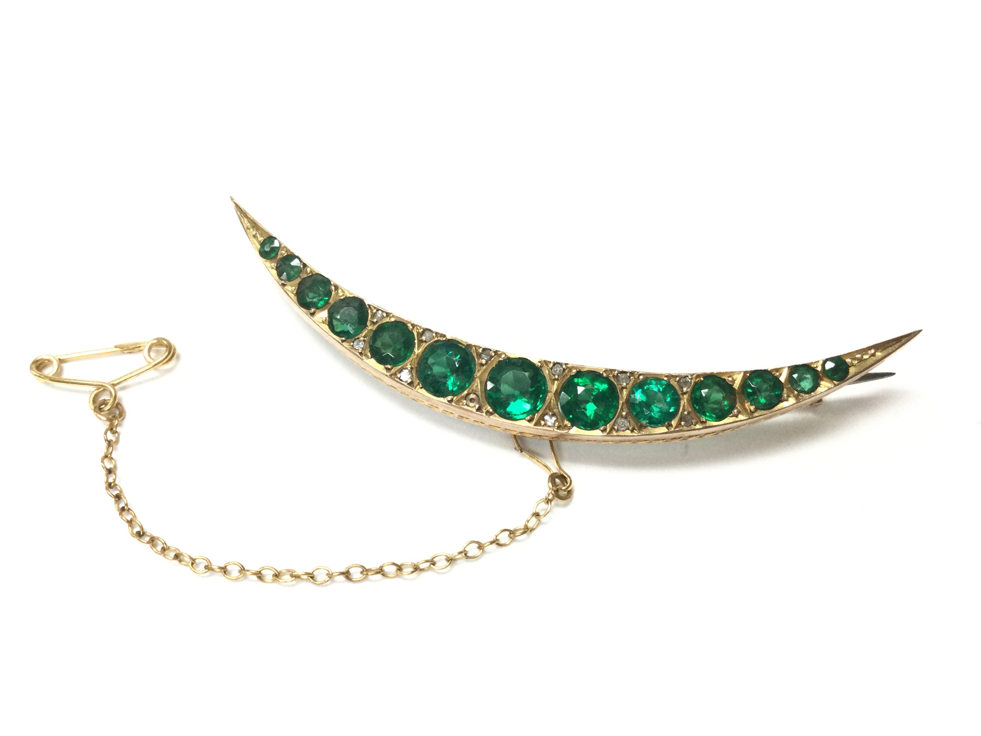 A 9ct gold Chester hallmarked crescent brooch set with small diamond shards and green sapphire. 4.8g total weight. Postage category A