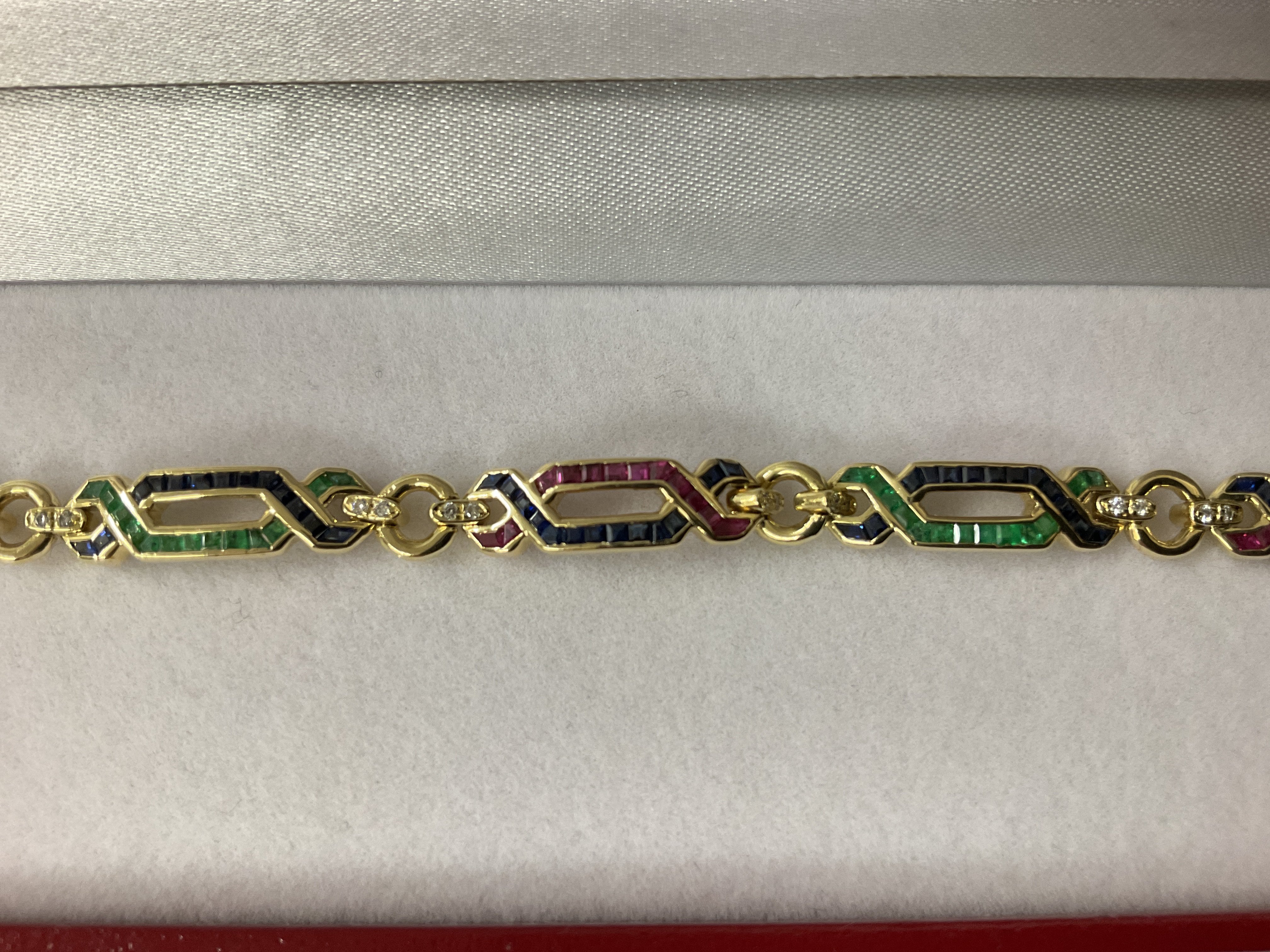 Exciting 18ct yellow gold ruby, emerald, sapphire and diamond &ldquo;figure of eight&rdquo; bracelet, boxed. Rubies 0.50ct approx. Sapphire 0.50ct approx. Emeralds 0.40ct approx. Diamonds 0.25ct. Postage category A.