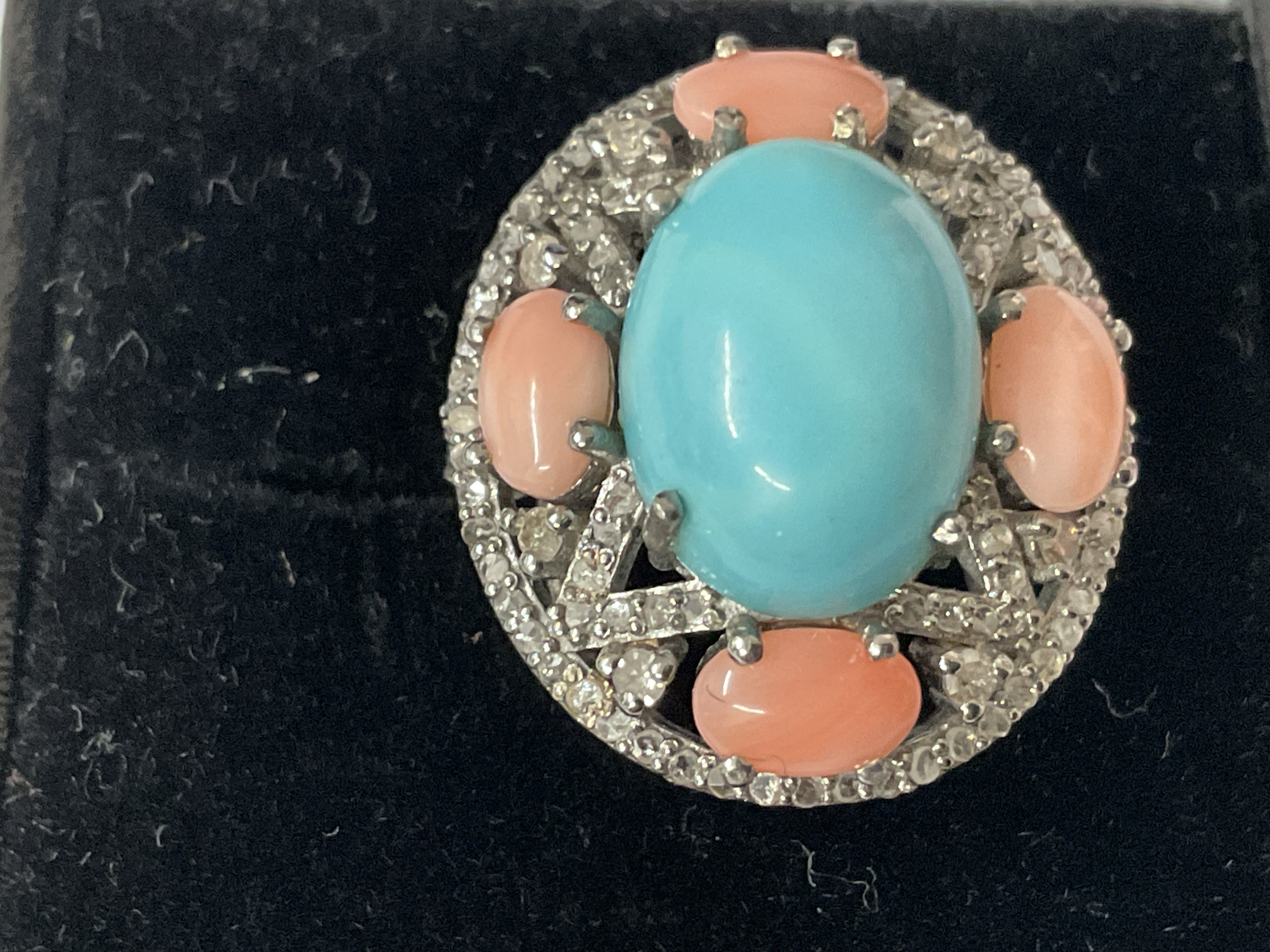 Large oval dress ring in white metal set with a central cabochon turquoise, 4 cabochon turquoise, 4 cabochon pink coral and mixed and rose cut diamonds, boxed. Turquoise 5.28ct. Coral 2.00ct. Diamonds 0.50ct. Ring size approx M. Postage catagory A.