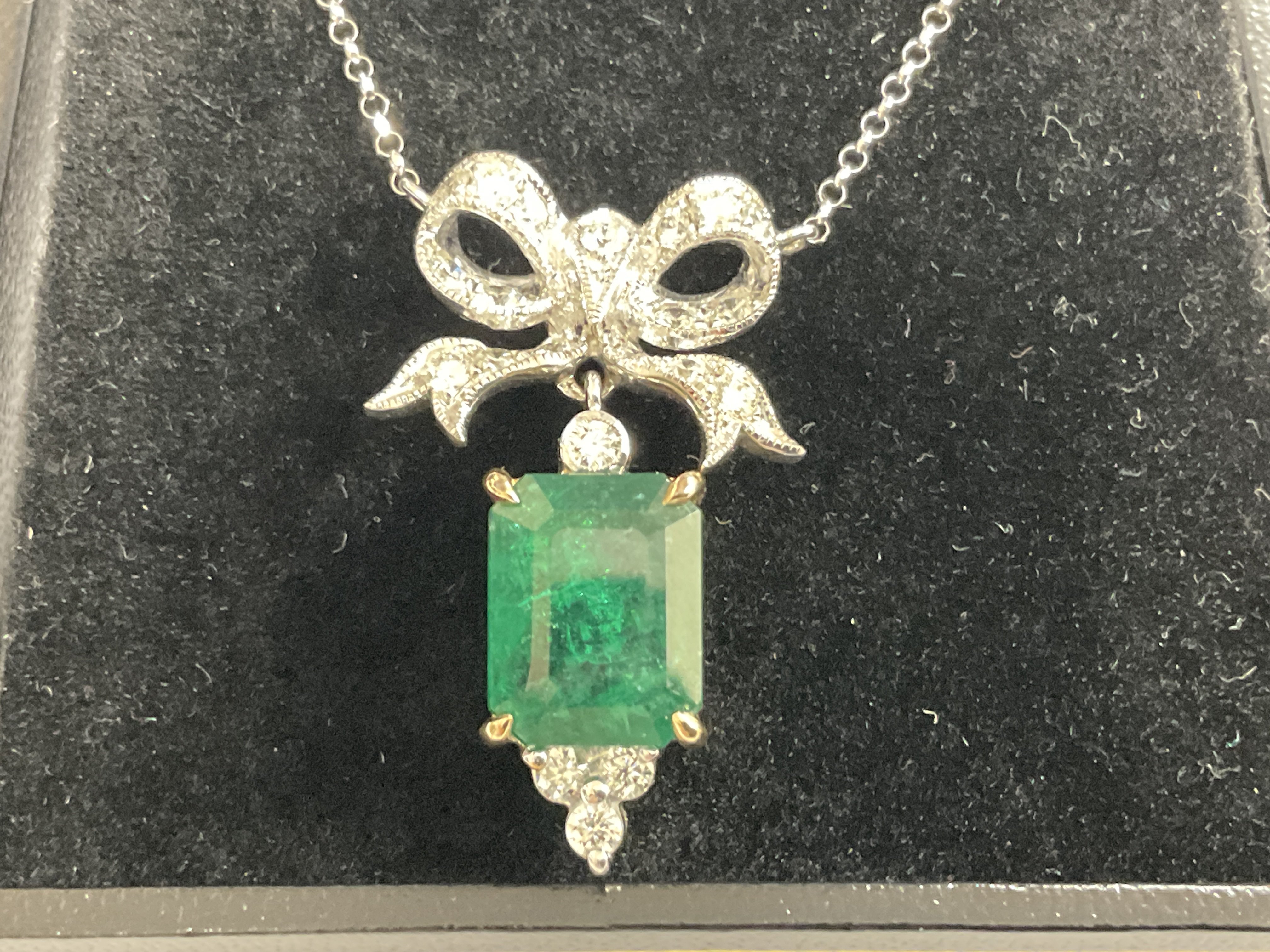 18ct white and yellow gold pendant set with a step cut emerald with RBC diamonds set below, and a diamond set large bow bale with integral 18ct white gold chain, boxed. Emerald 4.59ct. Diamonds 0.74ct. Postage category A.