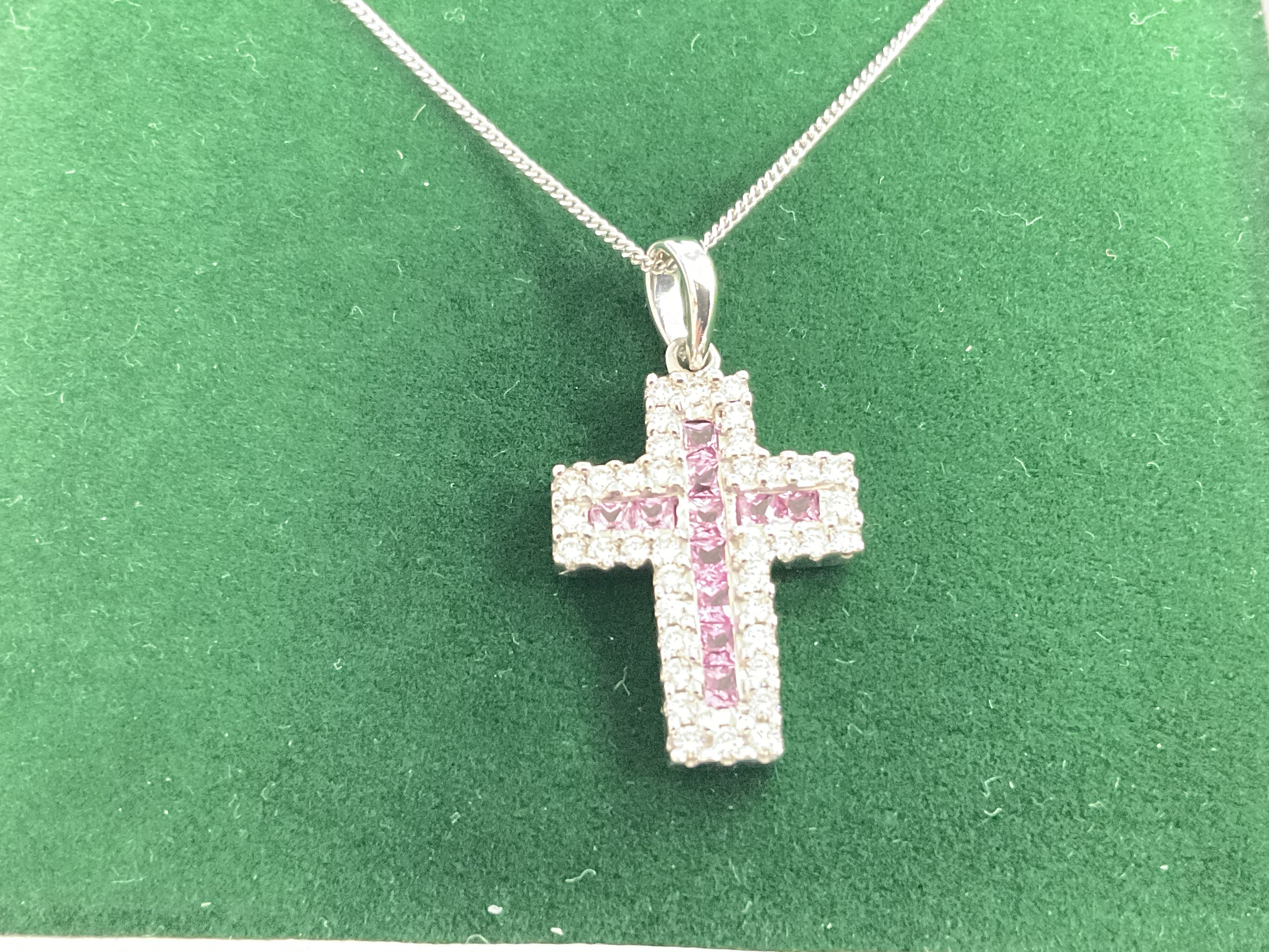 18ct white gold cross set with square cut pink sapphires and RBC DIAMONDS KN AN 18 ct white gold chain, boxed. Sapphires 0.30ct approx. Diamonds 1.00ct approx. Postage category A.