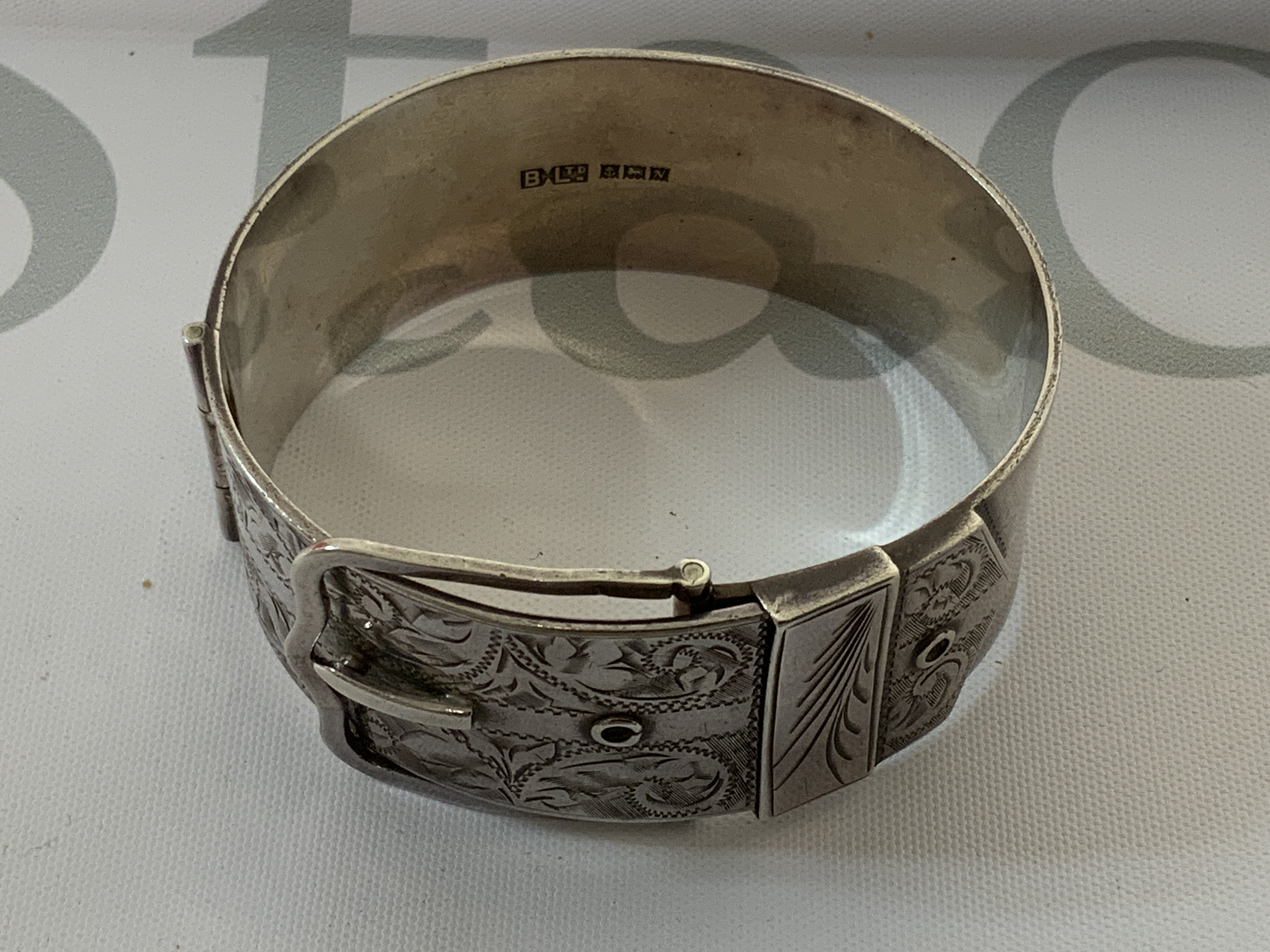 A heavy hallmarked silver buckle design bangle, with silver pill box. (A) 69g.