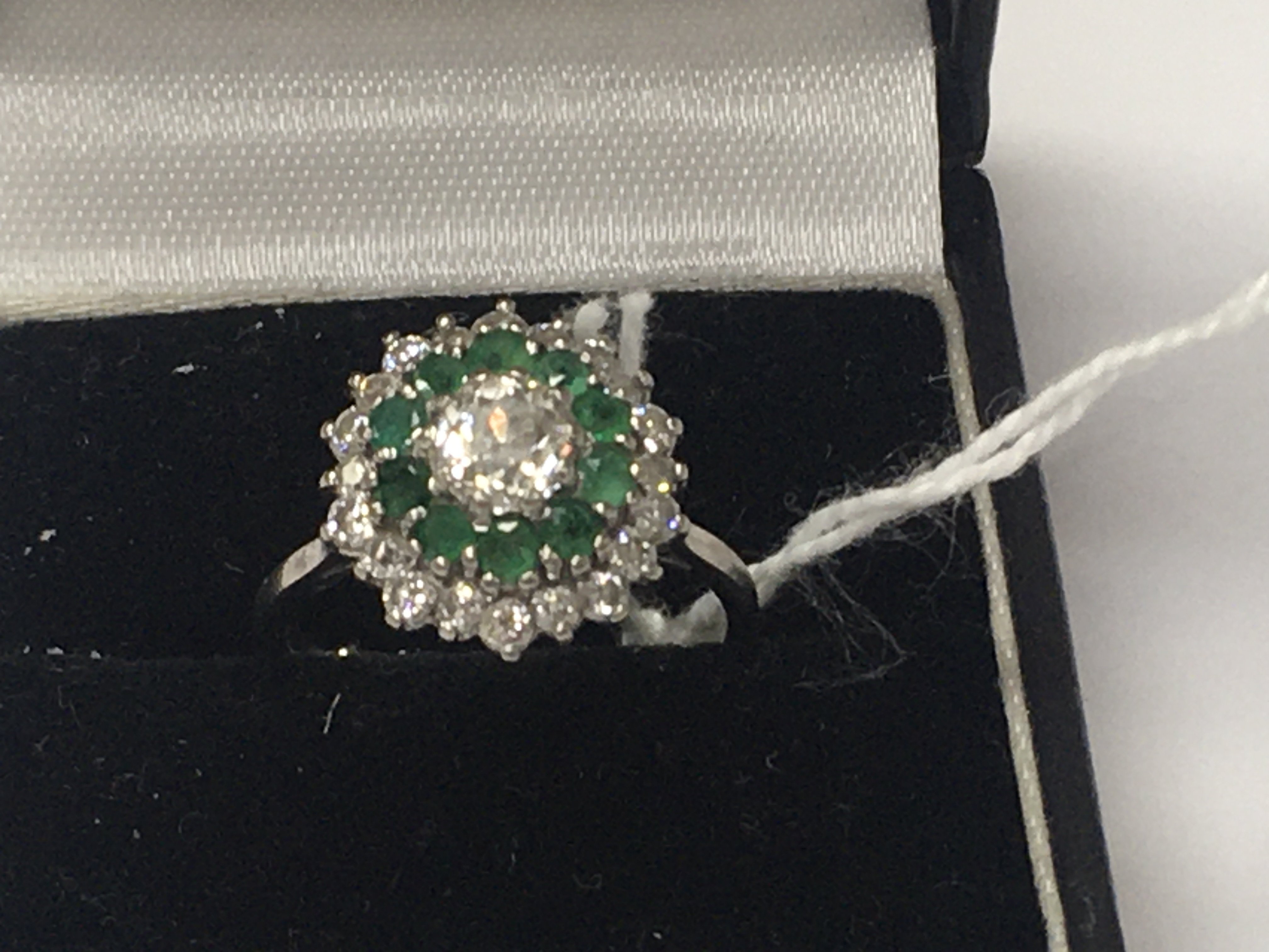 A 18 ct white gold ring inset with central diamond surrounded by emeralds and further diamonds. Size J