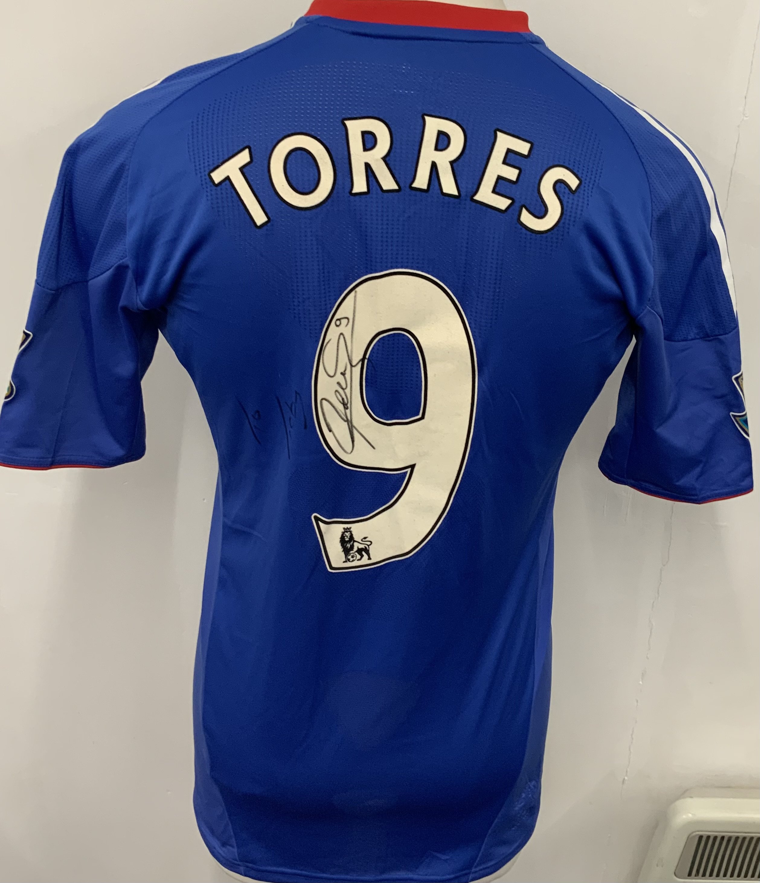 Chelsea 2010 - 2011 Match Worn Torres Football Shirt: Blue short sleeve home shirt with Gold Premier League sleeve badging stating Champions 09/10. Signed to rear with dedication. Number 9 Torres to reverse. 