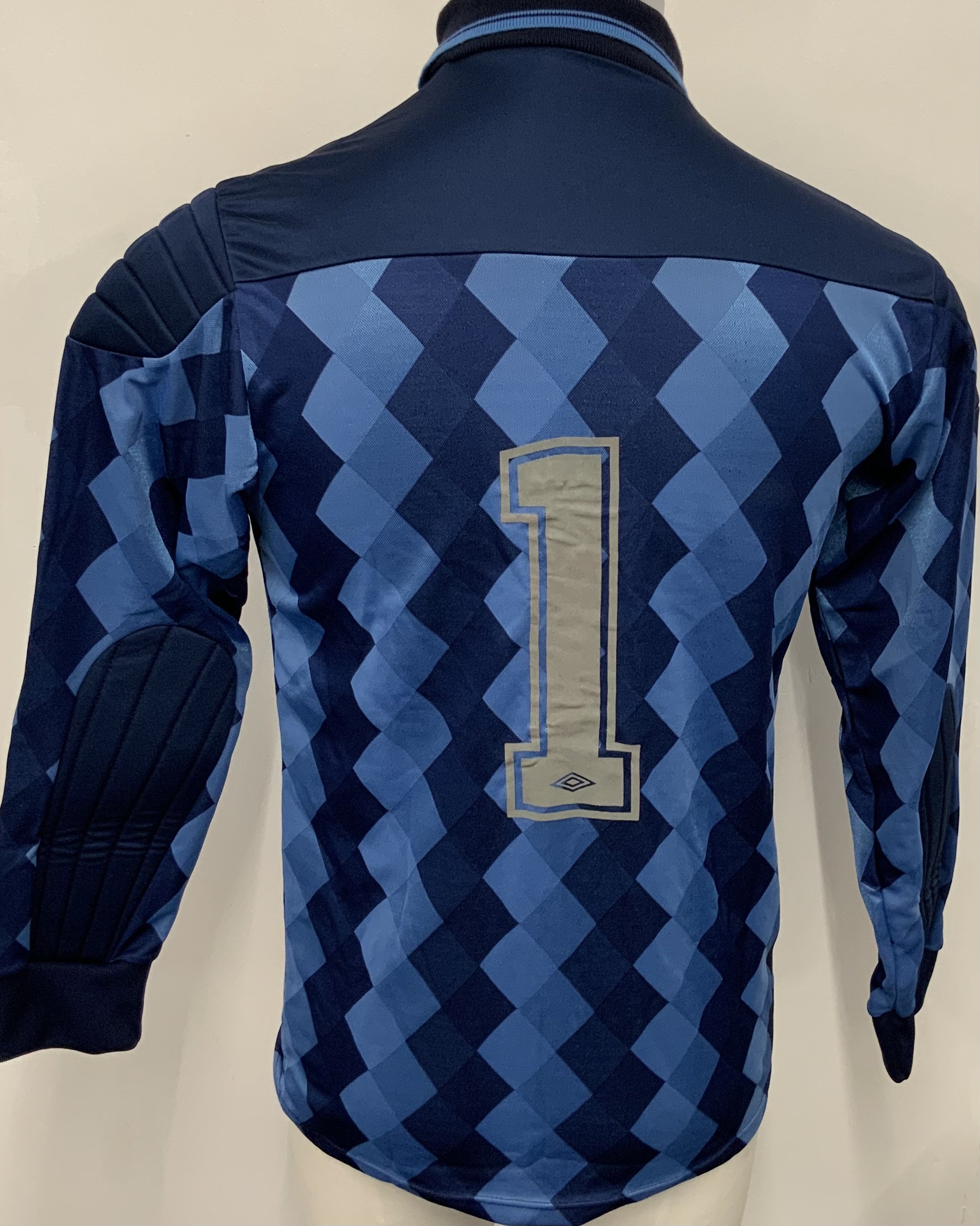 England 1989 Signed Football Shirt: Blue long sleeve Umbro goalkeeper shirt with number 1 to rear. Signed by Peter Shilton and a signed photo of him wearing the shirt is included. Shilton wore this shirt at a photo shoot to promote his record 109th cap. Not match worn. 