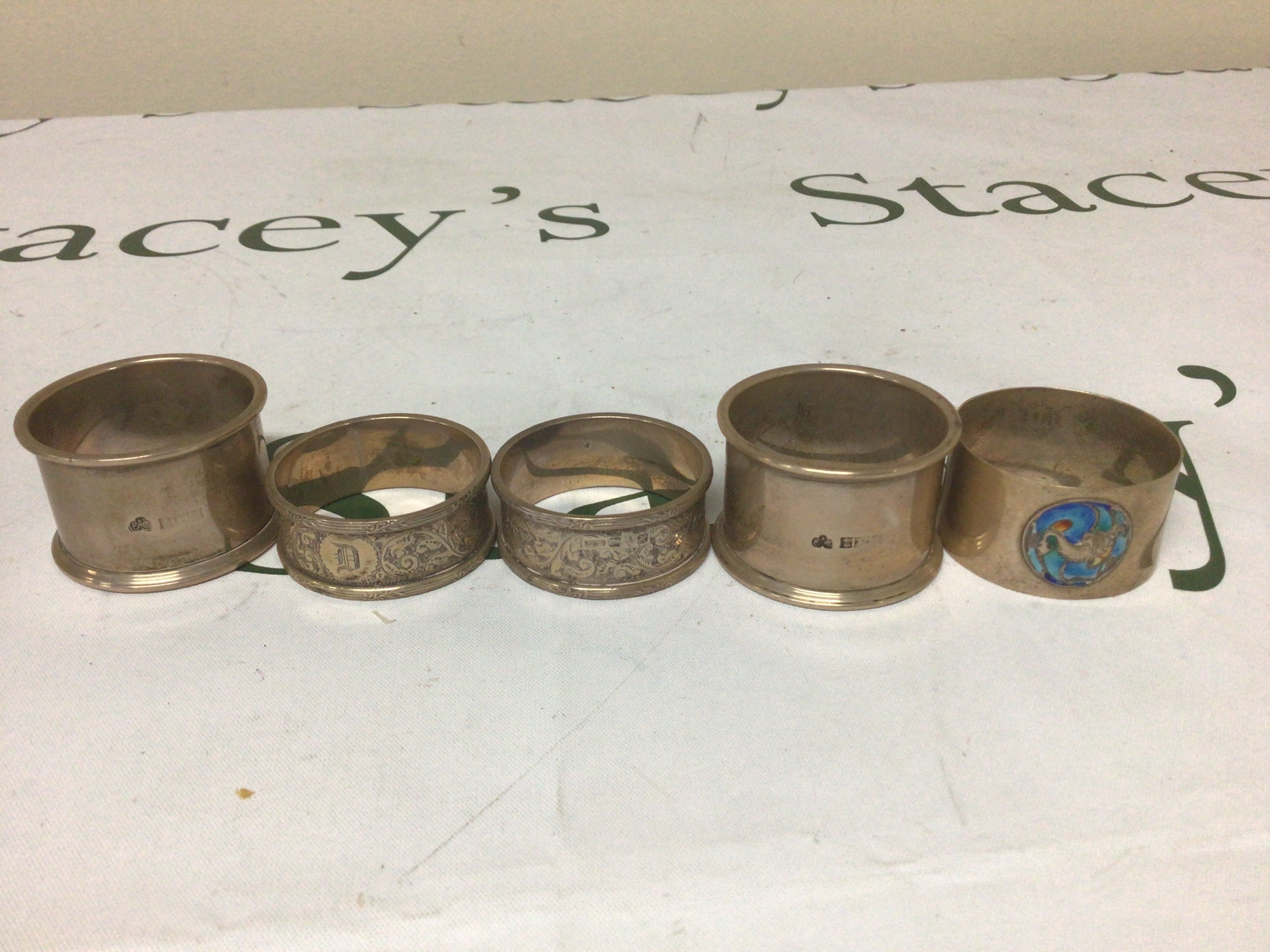 A collection of five silver napkin rings one decorated with applied enamel. Weight 146g