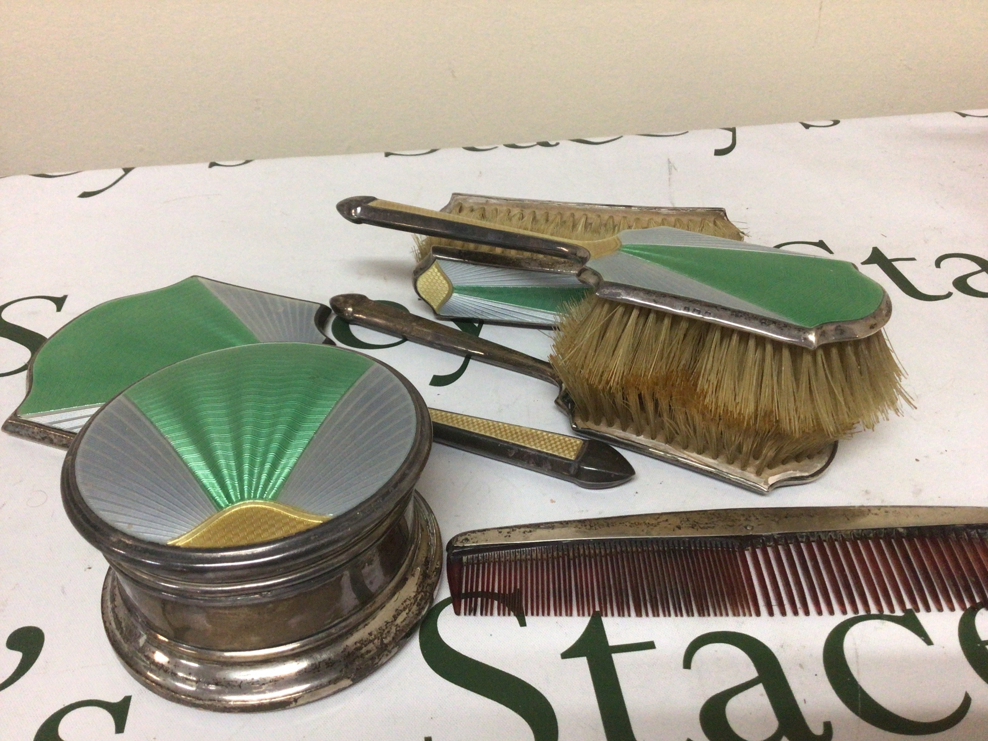 A Silver and enamel Art Deco dressing table set comprising a silver box of circular shape with tricolour enamel mirror sets of brushes and a comb.