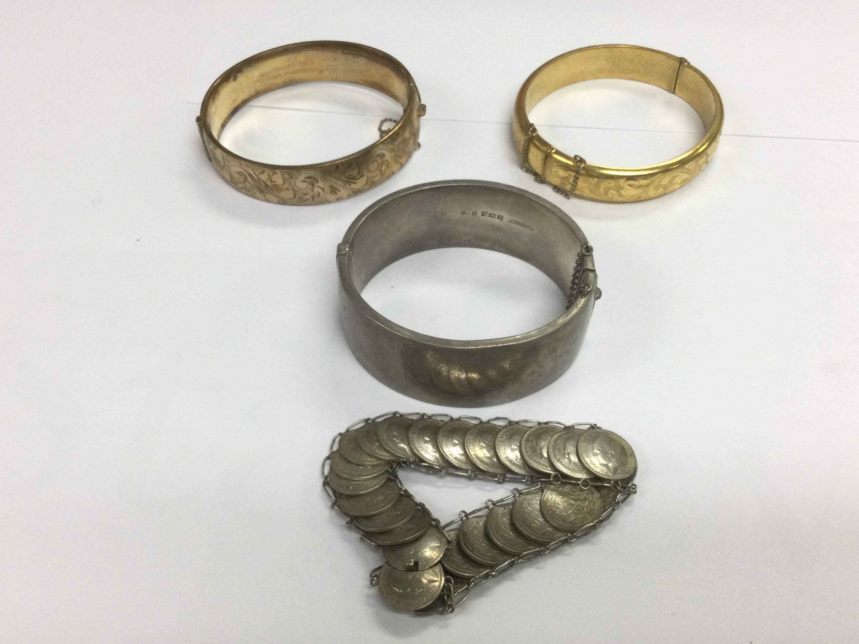 Two gold plated bangles, a silver bangle and a coin bracelet. Shipping category A.