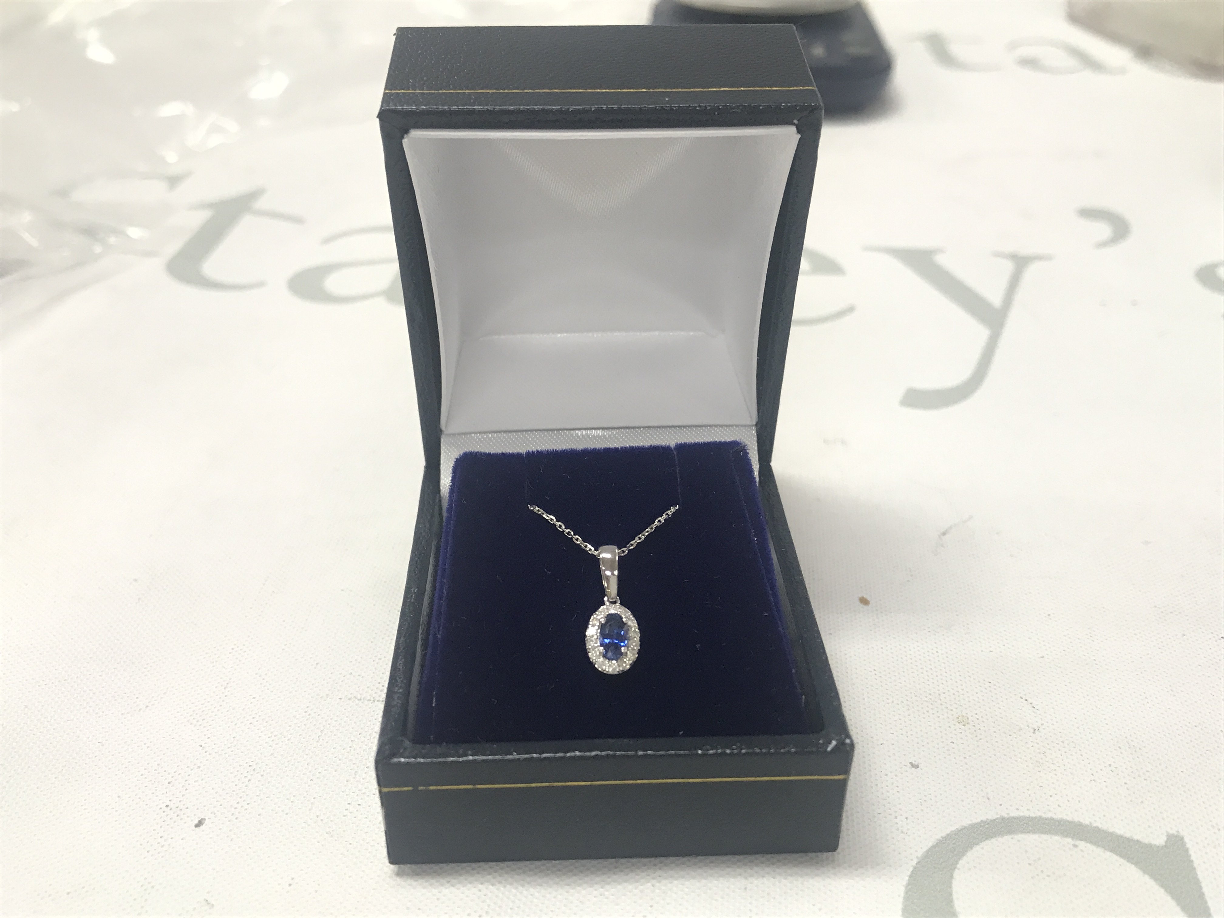 9ct white gold oval sapphire and RBC diamond cluster pendant on a 9ct white gold chain, boxed. Sapphire 0.39ct. Diamonds 0.07ct.