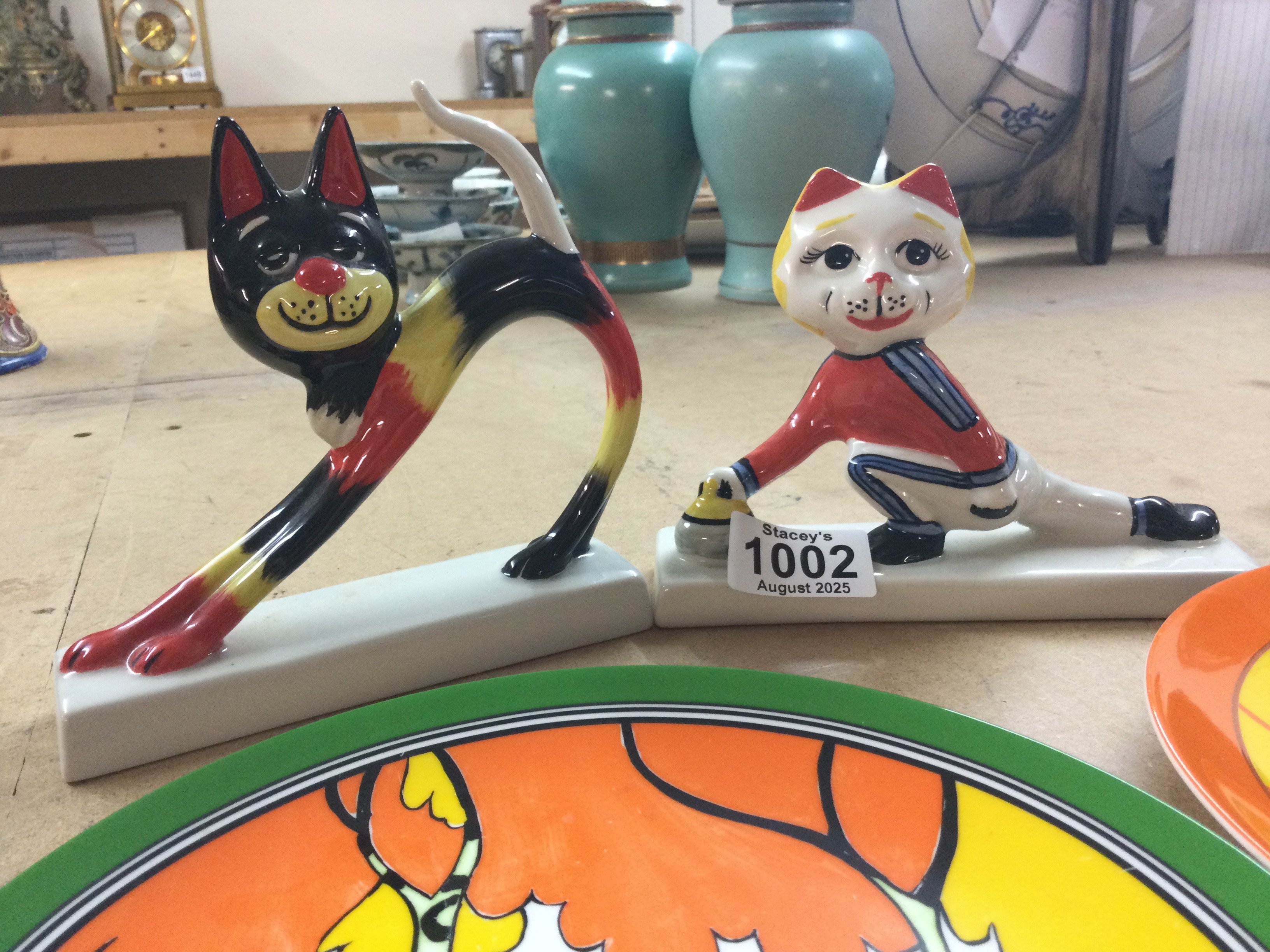 Two Art Deco style L Bailey cats together with three Wedgwood Clarice cliff plates .