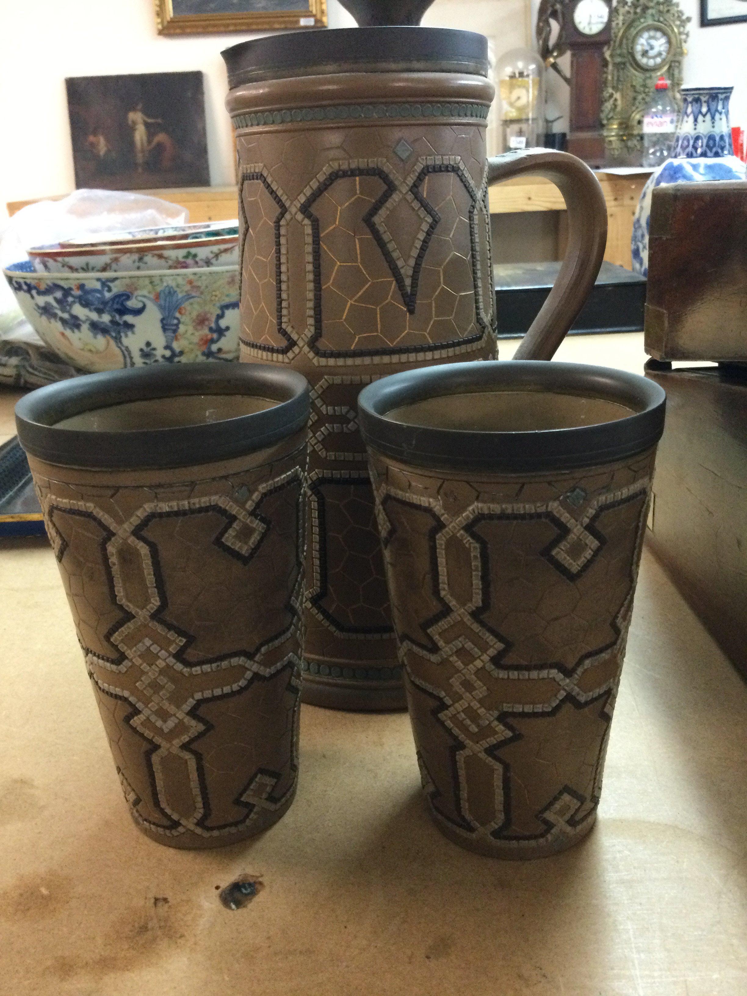 A Doulton jug with a silver plated rim and a pair of matching beakers .