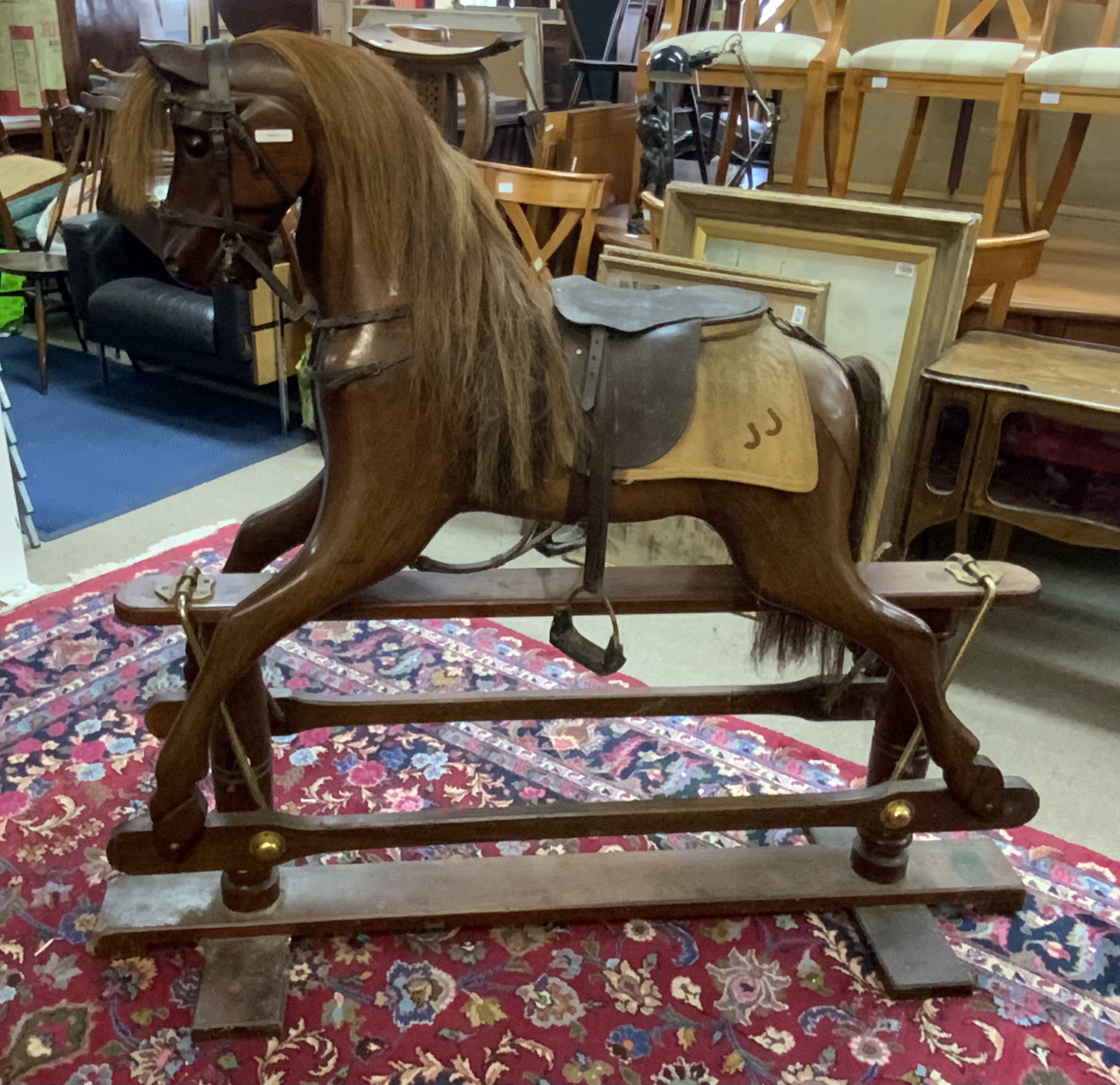 A large carved mahogany rocking horse with leather saddle and horse blanket, in need of attention. 129cm x 147cm x 47cm.