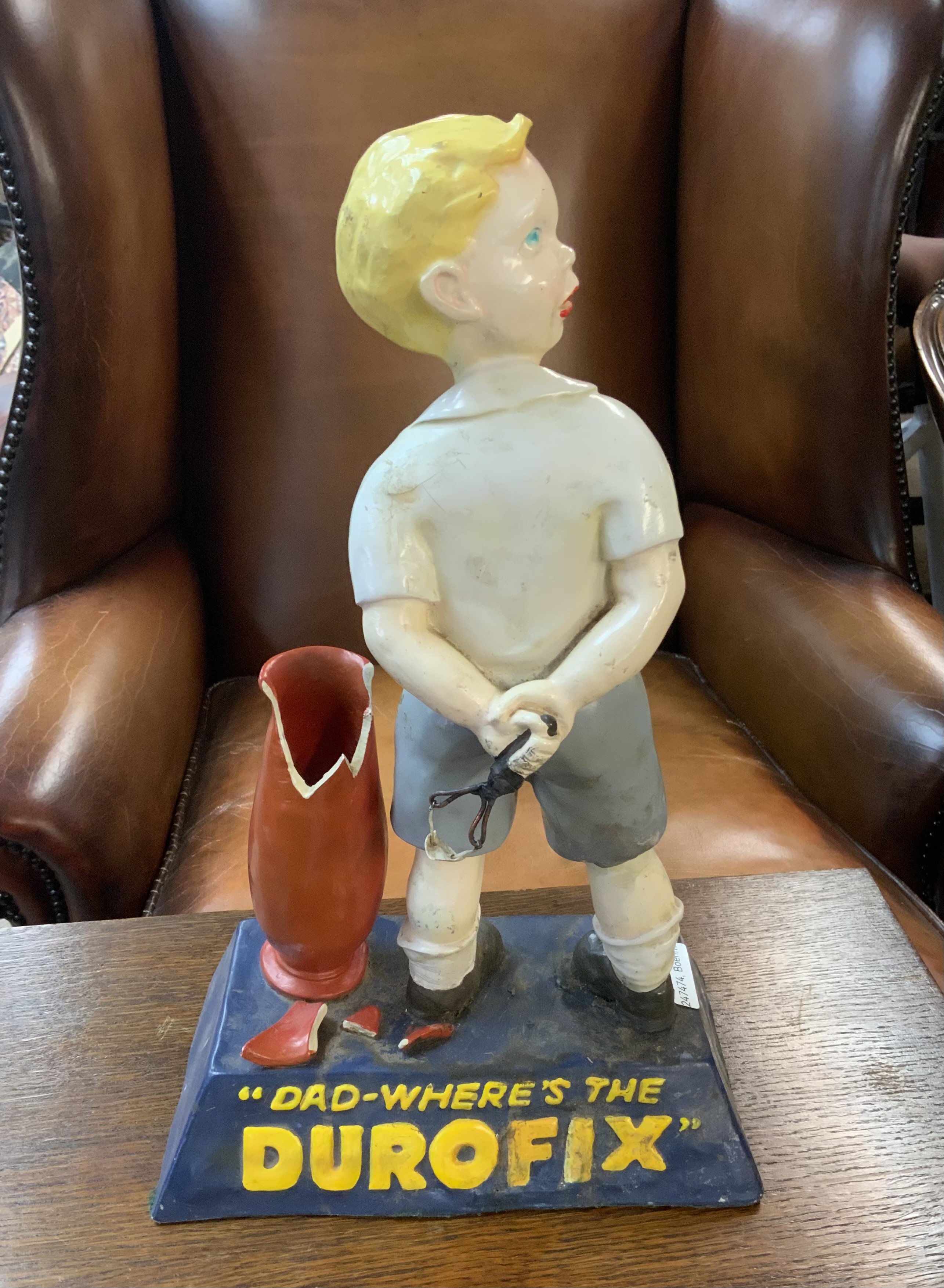 Advertising shop display figure, "DAD- WHERE'S THE DUROFIX", depicting a young boy with his arms behind his back holding a catapult and with a broken vase to his left, 24.5cm wide, 38cm high