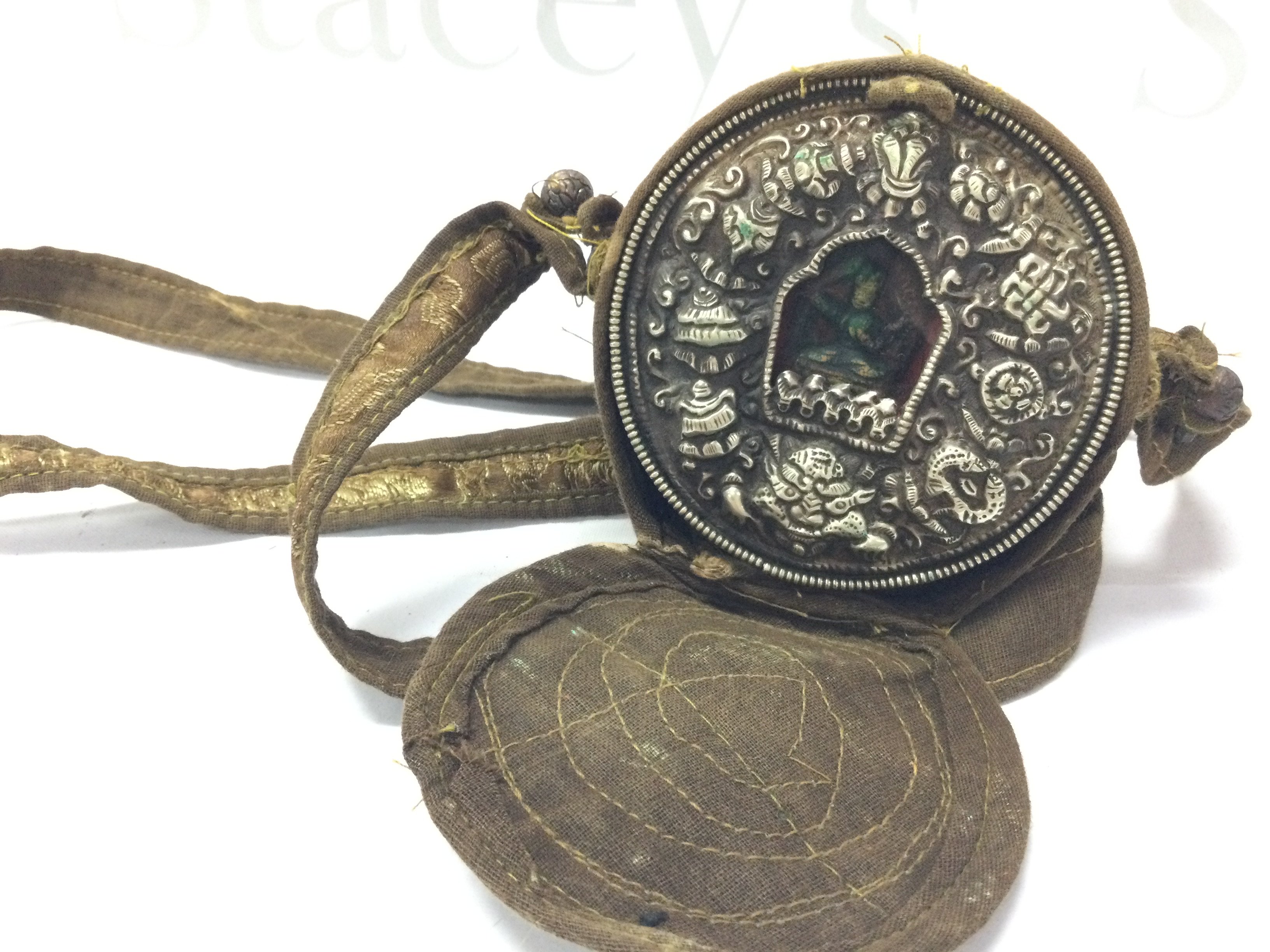 A small Tibetan travelling shrine with a silver embossed front and carrying bag . 8.5cm tall and wide.postage category B