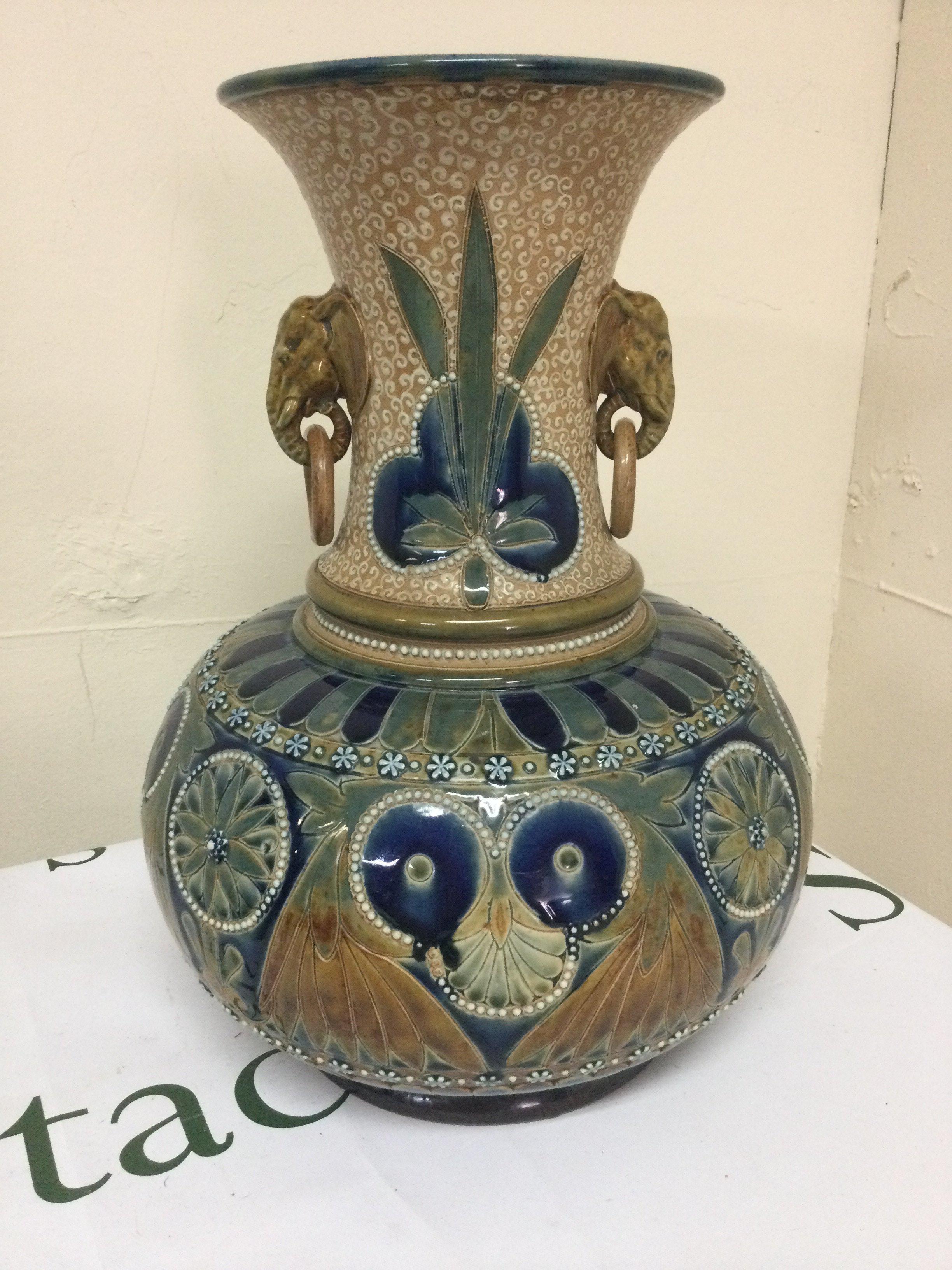 A unusual Florence Barlow Doulton Lambeth stoneware Art pottery vase decorated with stylistic Flowers and foliage with elephant ring handles in a blue green brown glaze . 32 cm. Three beads missing.
