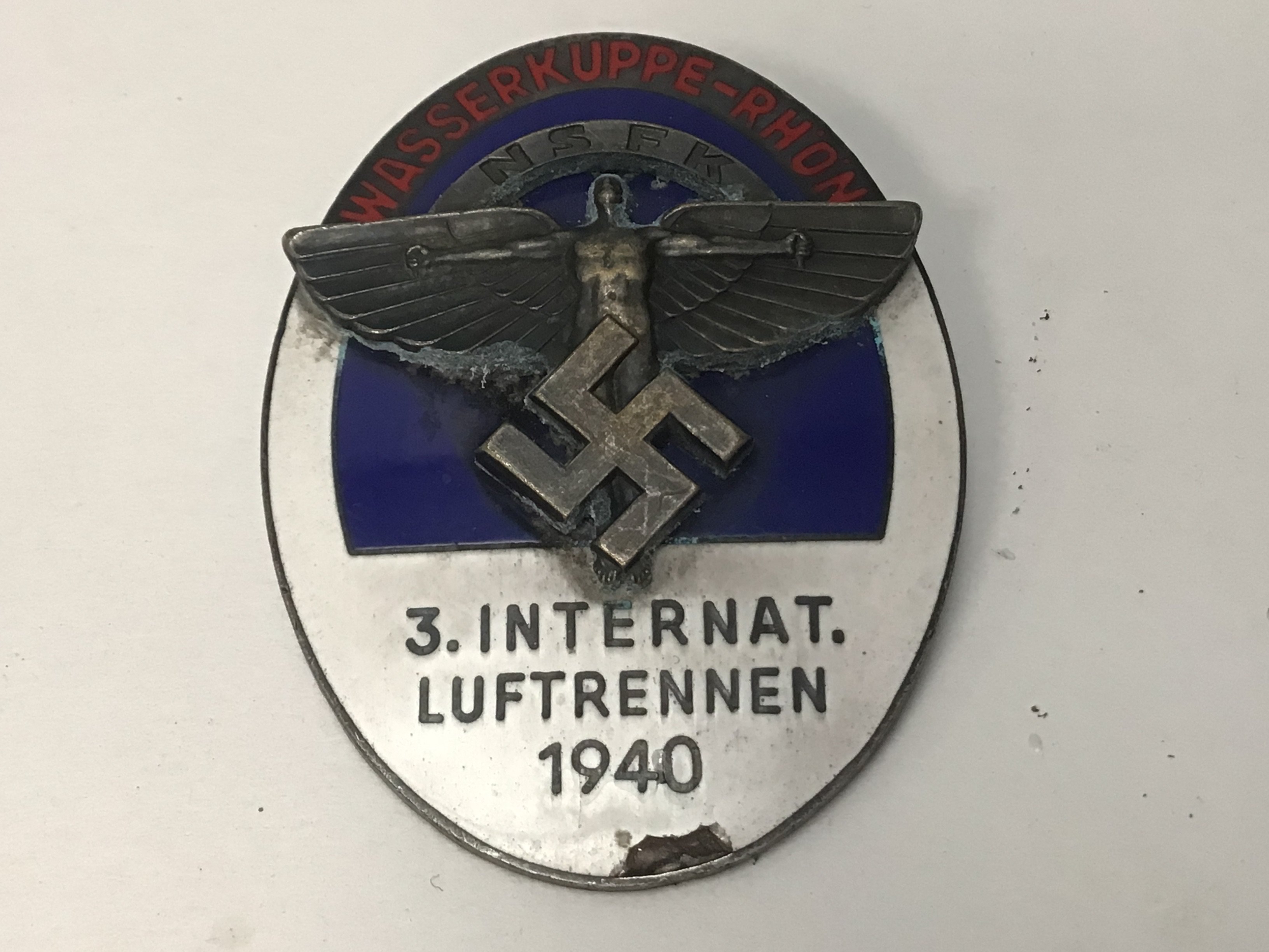 A Third Reich oval enamelled NSFK pin back badge, for &ldquo;3. Internat. Luftrennen 1940, Wasserkuppe Rhon&rdquo;, with white, blue and red enamel and superimposed NSFK device in the centre, the back embossed &ldquo;Ges Gesch&rdquo; GC Minor damage to the enamel