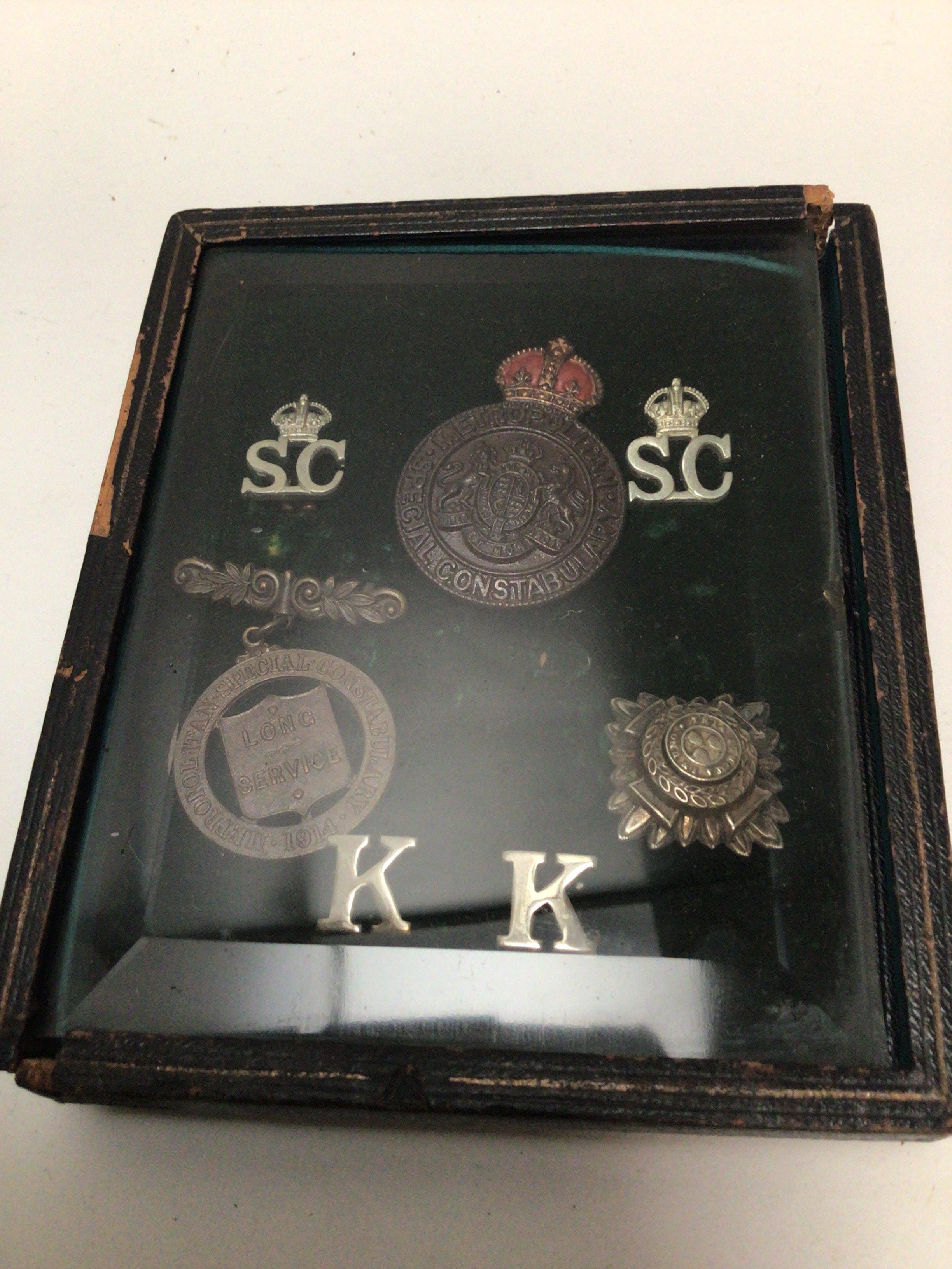 A damaged leather and glass case containing early 20th century Metropolitan Police badges possible Kings Coronation body Guard
