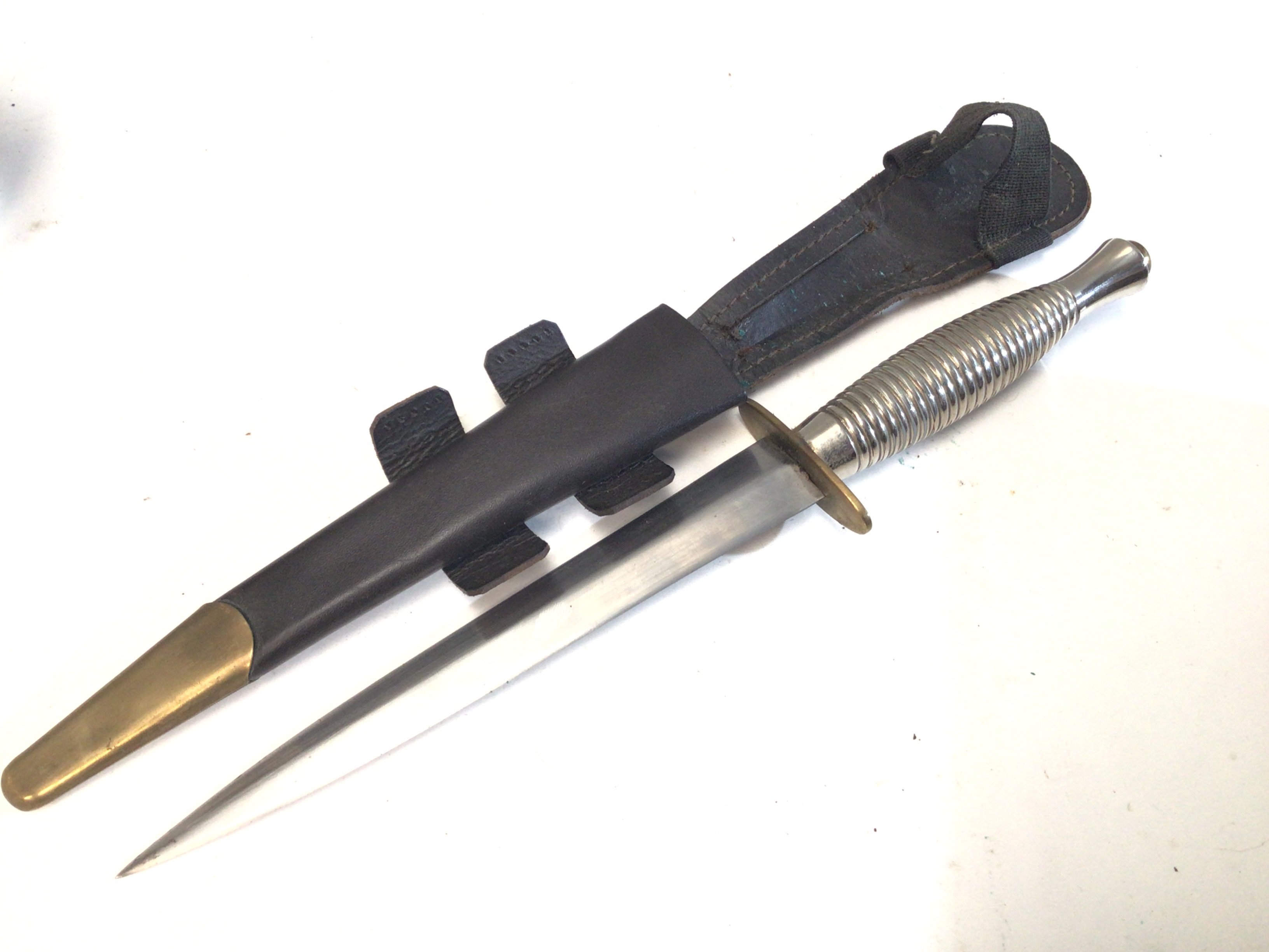 A Fairbrain Sykes Commando Knife Chrome finish made in Sheffield type 3. The brass cross guard with makers Stamp. leather scabbard..