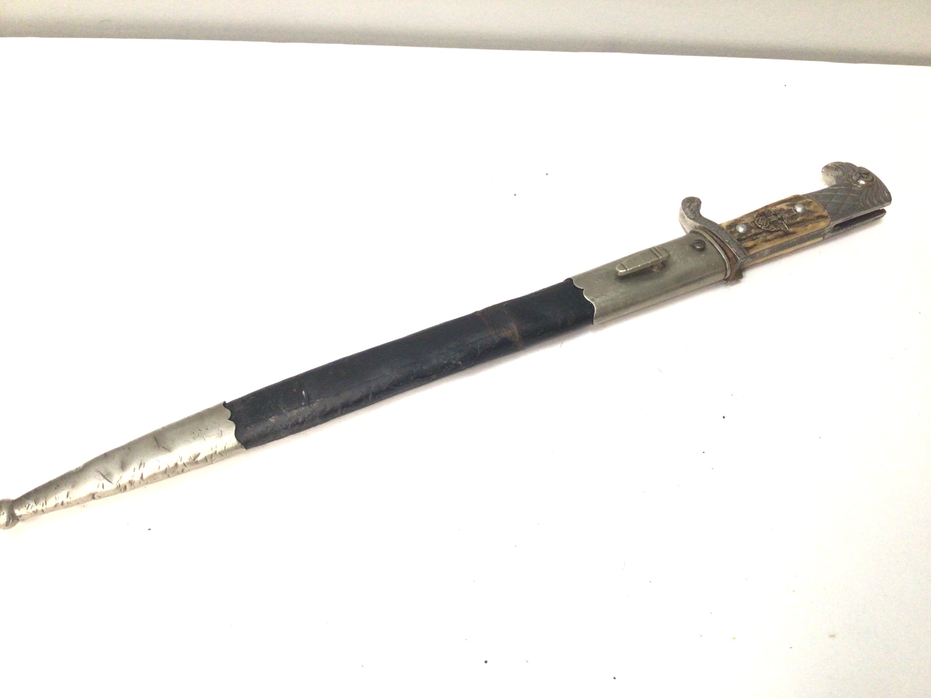 A genuine and good example of a German Third Reich Police dress bayonet with horn grip applied badge eagle top the blade with number to the edge 357 and makers stamp mark leather and metal scabbed blade has few marks condition in keeping with age.